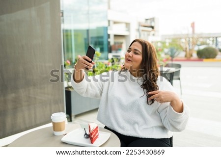 Attractive fat woman working as a content creator filming a social media story with her smartphone while at the coffee shop