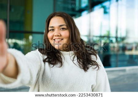 Personal perspective of a latin beautiful fat woman smiling while making eye contact taking a selfie in the city