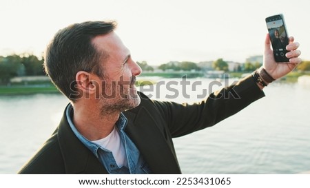 Close up, man makes video call on mobile phone on the embankment of the river. Backlight