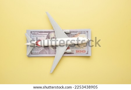 Flatlay picture of toy aeroplane with fake money on yellow background. Expensive flight fare.