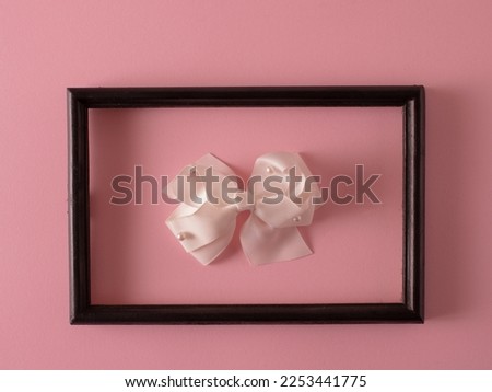 A black picture frame hanging on a pink wall with a white pearl 
