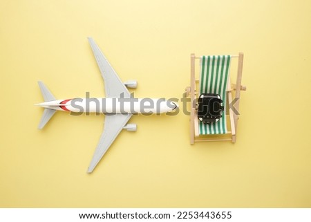 Flatlay picture of toy aeroplane , folding beach chair and suitcase on yellow background.