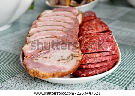 In the picture, slices of chopped meat and sausage lie in rows on a square plate.
