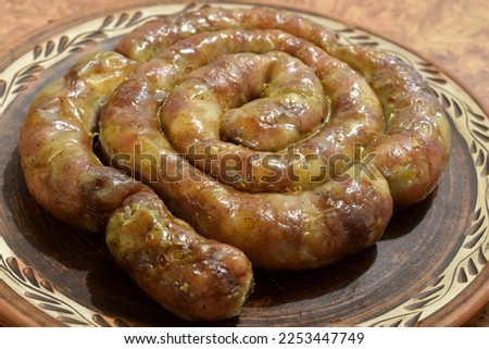 The picture shows a round clay plate on which sausages made at home lie in rings.