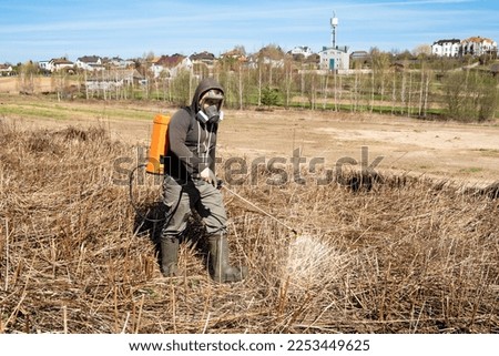 Farmer spraying pesticides and protects field from weeds and tick. Man with spray tank equipment. Tillage from ticks and insects. Springtime farm work. Dry grass. Water jet. Manual labor. Garden care.