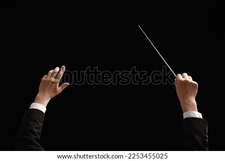 Back view of professional conductor with baton on black background, closeup Royalty-Free Stock Photo #2253455025