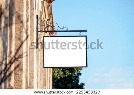 Blank signboard mockup hanging on the wall of the store in the street