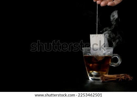 Glass of hot tea with tea bag hanging black background copy space, and cinnamon stick