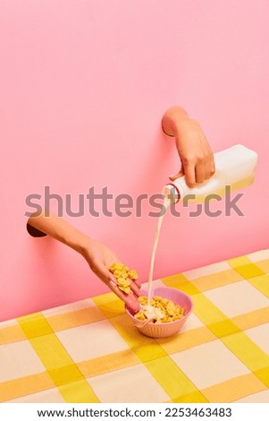 Food pop art photography. Female hands sticking out pink paper, pouring milk into bowl with corn flakes. Ordinary breakfast. Taste, creativity, art. Complementary colors. Copy space for ad, text