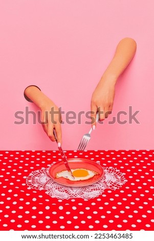 Food pop art photography. Female hand sticking out pink paper and cutting fried eggs on plate on retro tablecloth. Breakfast time. Taste, creativity, art. Complementary colors. Copy space for ad, text