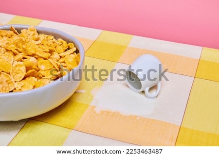 Food pop art photography. Bowl with cereal, corn flakes on yellow tablecloths with milk jar and spilled milk. Breakfast time. Taste, creativity, art. Complementary colors. Copy space for ad, text
