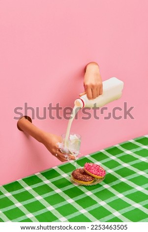 Food pop art photography. Female hands sticking out pink paper, pouring, spilling milk into cup. Donuts on green tablecloth. Concept of creativity, art. Complementary colors. Copy space for ad, text