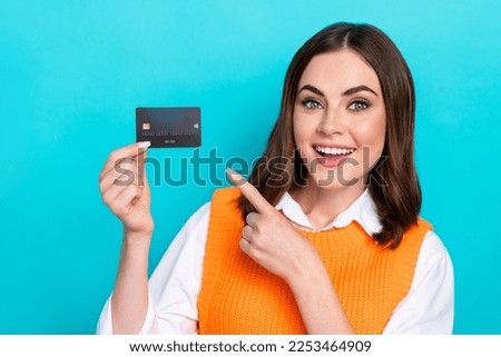Photo of cheerful satisfied adorable woman brown hair wear orange waistcoat directing at plastic card isolated on teal color background
