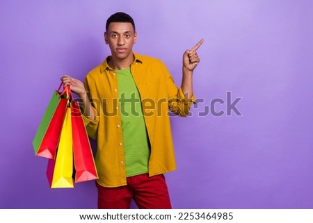 Portrait of handsome satisfied guy wear yellow clothes holding shopping bags indicating empty space isolated on violet color background
