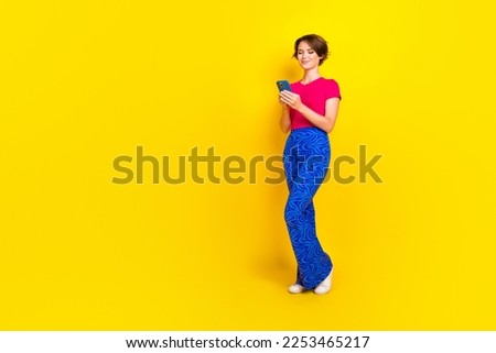 Full length photo of adorable cute lady stylish clothes hold device write post stand near empty space isolated on yellow color background