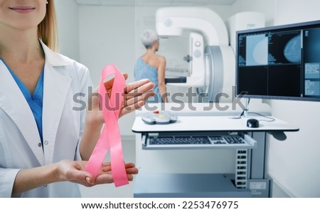 Mammologist showing breast cancer awareness ribbon in mammography room, urging women to have regular breast exams. Fight against breast cancer Royalty-Free Stock Photo #2253476975