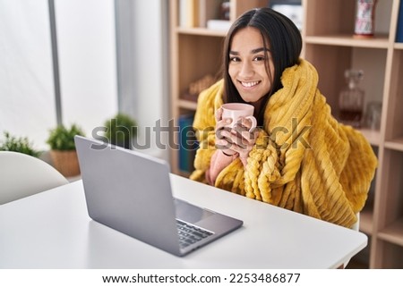 Young hispanic woman using laptopo drinking coffee at home