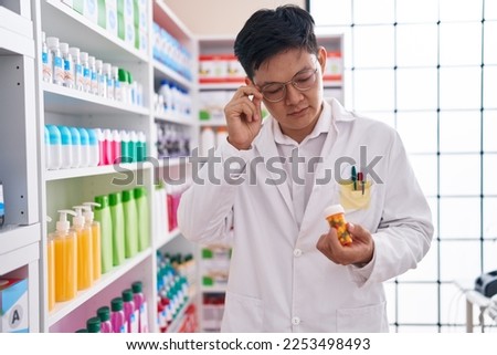 Young chinese man pharmacist looking pills bottle at pharmacy