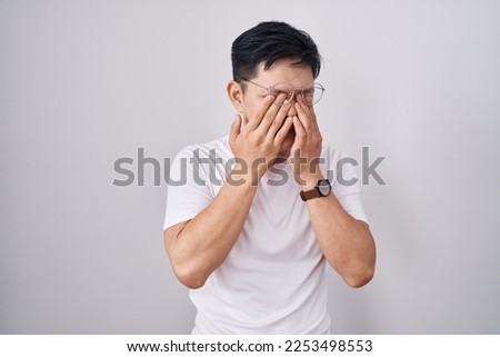 Young asian man standing over white background rubbing eyes for fatigue and headache, sleepy and tired expression. vision problem  Royalty-Free Stock Photo #2253498553