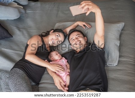 smiling father and mother taking a selfie with their baby in bed Royalty-Free Stock Photo #2253519287