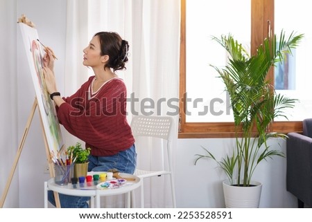 Creative of art concept, Young asian woman sit on chair and use paintbrush to painting on canvas.