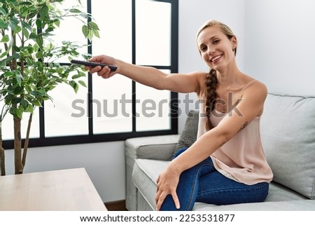 Young caucasian woman watching tv sitting on sofa at home