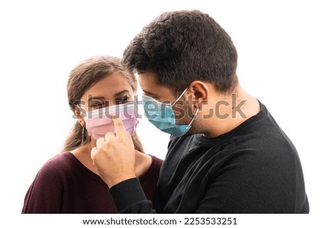 Cute man wearing blue protective face covering touching girlfriend nose with index finger through pink medical or surgical disposable mask isolated on white background Royalty-Free Stock Photo #2253533251