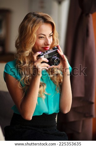Beautiful young woman photographer taking pictures with retro film camera, indoors