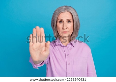 Photo of confident retired lady wear violet clothes demonstrate arm palm stop keep distance isolated on blue color background