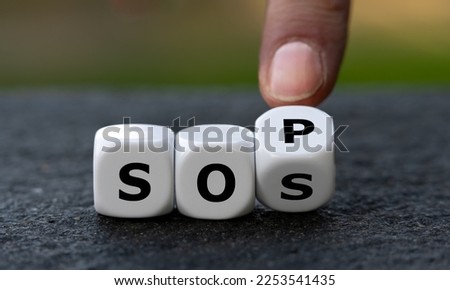 Hand turns dice and changes the abbreviation SOS (save our souls) to SOP (standard operating procedure). Symbol for getting help. Royalty-Free Stock Photo #2253541435