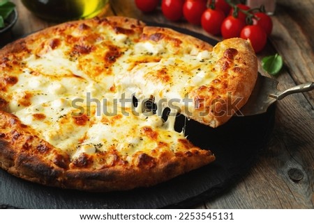 A slice of hot Italian pizza with stretching cheese. Pizza four cheeses with basil on a wooden background.