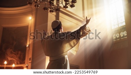 The Pope Stands Raises his Hands In A Gesture Of Universal Blessing, as He is being Luminated by the Guidance of God. He is Lifting His Hands Towards Heaven As A Sign Of Utter Devotion To the Lord