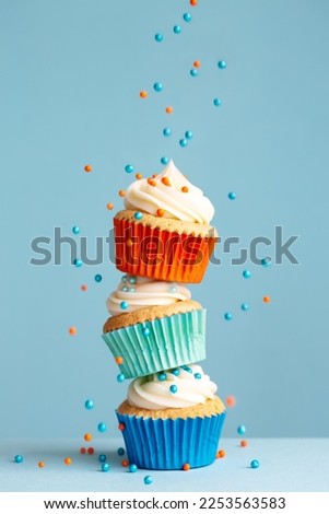 Sugar sprinkles falling on stack of colorful cupcakes Royalty-Free Stock Photo #2253563583