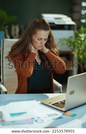 stressed elegant small business owner woman with laptop and neck pain in the modern green office. Royalty-Free Stock Photo #2253578901