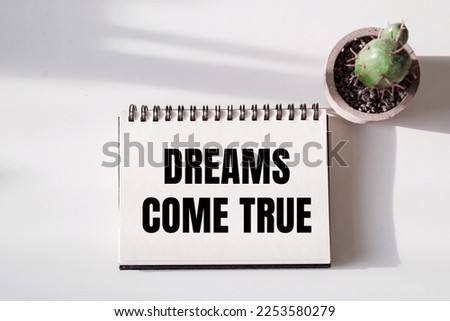 DREAMS COME TRUE text on notepad on a white desk with cactus Royalty-Free Stock Photo #2253580279