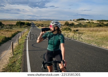  Female cyclist a gravel bike drinks water during exercise.Empty city road. Sports motivation.Murcia region in Spain