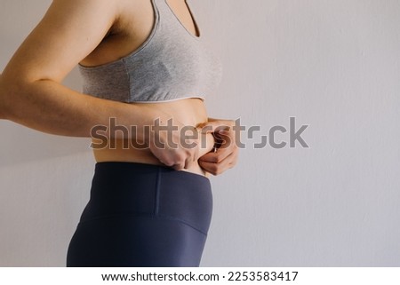 Beautiful fat woman with tape measure She uses her hand to squeeze the excess fat that is isolated on a white background. She wants to lose weight, the concept of surgery and break down fat under the Royalty-Free Stock Photo #2253583417
