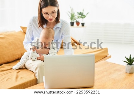 Young single mother mom with toddler newborn baby infant son using laptop, searching web, watching cartoons together. Working from home on maternity leave, freelancer, looking for kids goods.