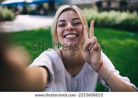 Close up selfie portrait of cheerful female showing v sign and smiling while enjoying travel lifestyle, happy Caucasian woman laughing at camera during leisure for creating influence content