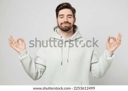 Young spiritual tranquil man wear mint hoody hold spread hands in yoga om aum gesture relax meditate try to calm down isolated on plain solid white background studio portrait. People lifestyle concept