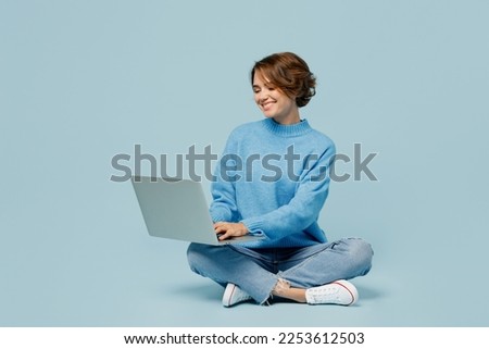 Full body young smiling happy fun cool IT woman wear knitted sweater hold use work on laptop pc computer isolated on plain pastel light blue cyan background studio portrait. People lifestyle concept Royalty-Free Stock Photo #2253612503