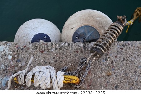 Rubber buoys on the pier and a yellow metal shackle with rope and spring for mooring ships. Royalty-Free Stock Photo #2253615255