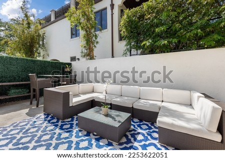 Elegant patio with outdoor furniture, wooden fence, stone beds, tropical plants, trees, glass doors, blue sky, located in fort lauderdale, miami, florida