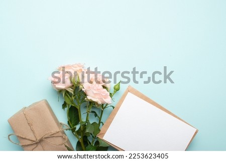 A bouquet of bush roses, a gift in kraft paper, a kraft envelope on a light blue background. Valentine's Day, birthday, March 8, Mother's Day. Space for copying. Flat position, top view.