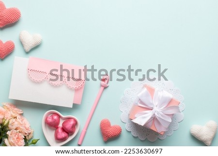 A gift with a bouquet of flowers and knitted hearts and a lace pink envelope, sweets in pink foil in the shape of a heart on a light blue background.