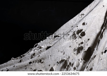 old dirty ragged cloth with holes, grunge damaged cloth veil on black background, ripped white fabric with many holes, copy space Royalty-Free Stock Photo #2253634675