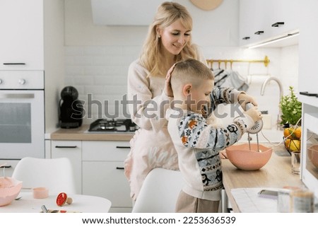Boy with his mother preparing chocolate cookies in a white kitchen. Light and airy modern photography. Having fun together, family time
