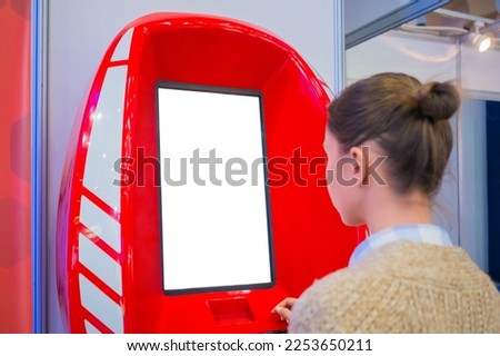 Woman looking at vertical digital interactive white display of kiosk at exhibition or museum with futuristic sci-fi interior. Mock up, copyspace, template, isolated, white screen, technology concept Royalty-Free Stock Photo #2253650211