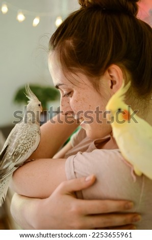 Love for animals.Girl with parrots.Beautiful cockatiel parrots.Woman with birds.Bird on the shoulder.Beautiful skin with freckles.Cute female smile.Care for animals.Exotic bird.Domestic parrots. Royalty-Free Stock Photo #2253655961