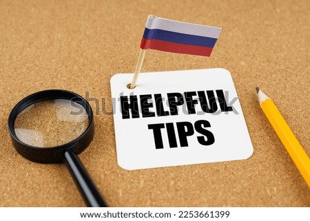 On the table is the flag of Russia, a pencil, a magnifying glass and a sheet of paper with the inscription - Helpful Tips